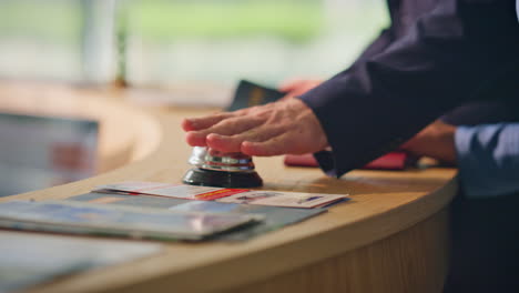 los huéspedes del hotel llegan a la recepción de cerca. la mano del hombre toca la campana en el mostrador del vestíbulo.