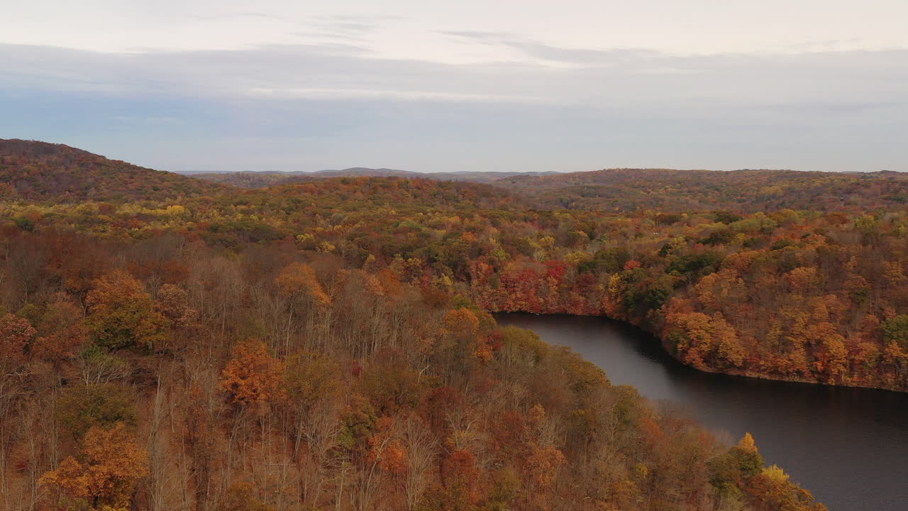 dolly aéreo sobre las copas de los árboles de color naranja de la temporada de otoño - montañas en un día nublado en la nueva presa de croton en el condado de westchester, nueva york