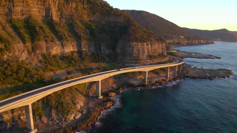 cars driving by the sea cliff bridge in nsw australia in sunrise - aerial shot