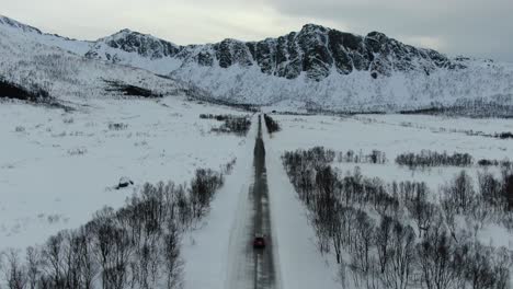 Drohnenansicht-In-Der-Gegend-Von-Tromsø-Im-Winter,-Die-Sich-Vom-Boden-Erhebt-Und-über-Eine-Schmale-Straße-Mitten-In-Einer-Verschneiten-Landschaft-Fliegt-Und-Einem-Auto-Von-Oben-In-Norwegen-Folgt