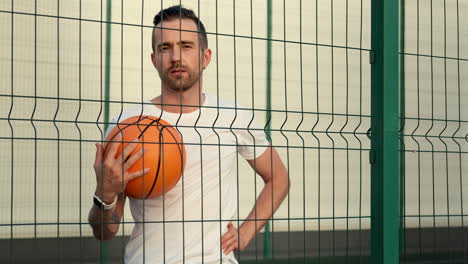 man holding basketball behind fence