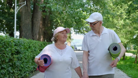 elderly couple walking in park with yoga mats