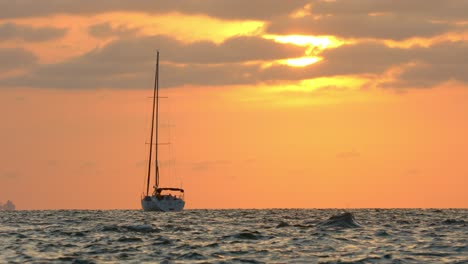 lonely sailboat anchored at open sea with orange horizon from evening sun in background, full frame slow motion