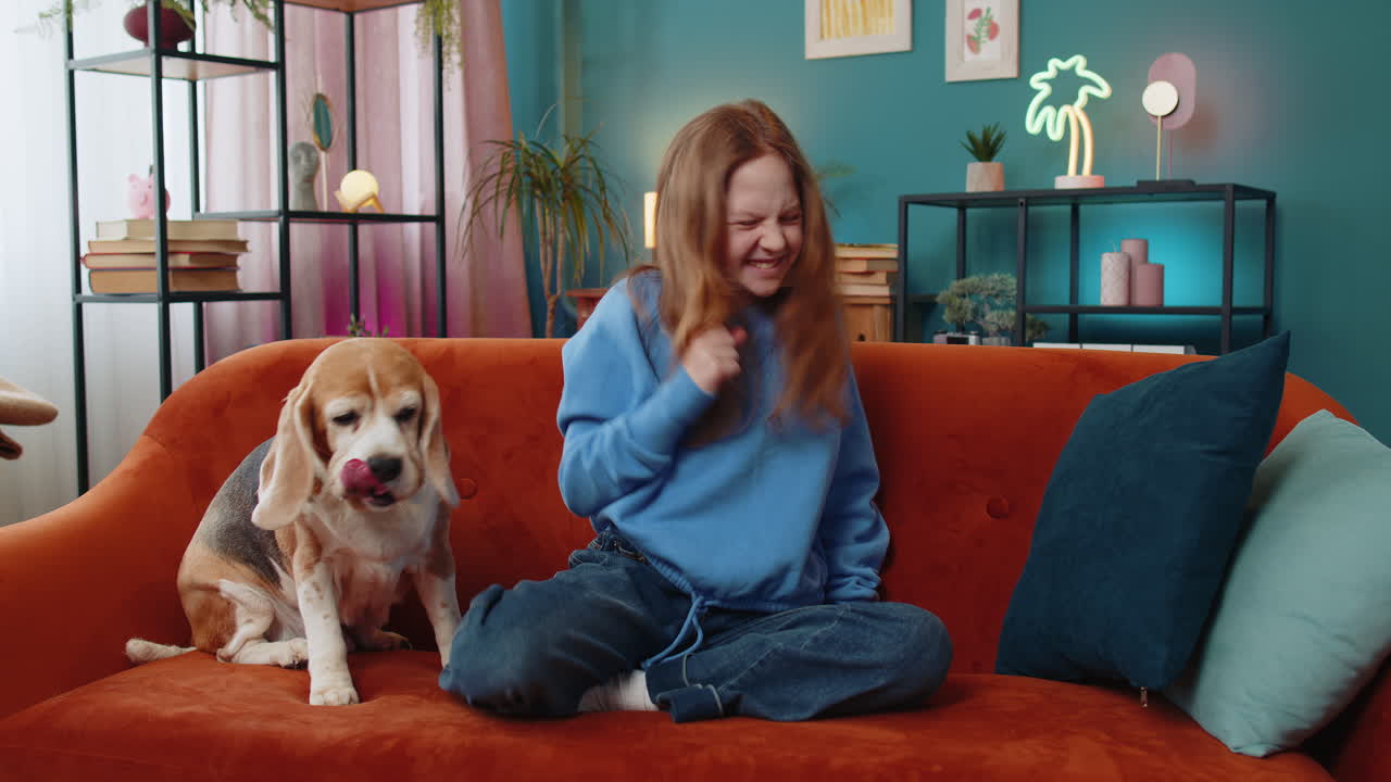 Cheerful young child girl celebrating victory winning the lottery at home beside beagle dog on sofa