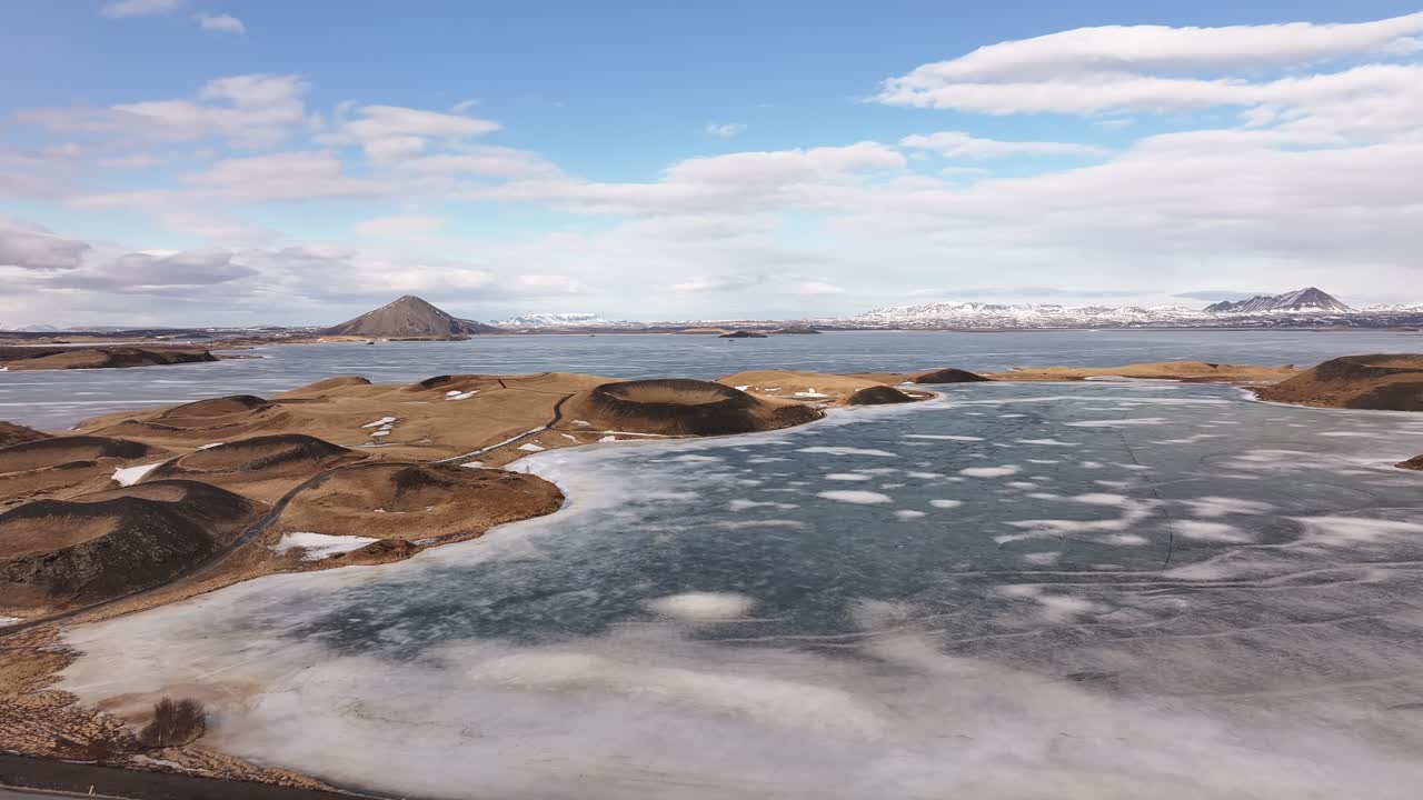 Frozen lake and craters in Mývatn, Iceland with snowy mountains in the distance