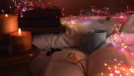 Cozy-background-of-an-open-book-on-a-bed,-next-to-a-mug-and-surrounded-by-colorful-christmas-lights