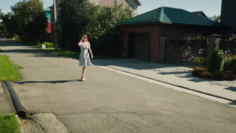 professional woman in patterned dress strolls confidently on quiet residential street under bright sunlight, enjoying calm weekend atmosphere with modern houses and lush greenery in background