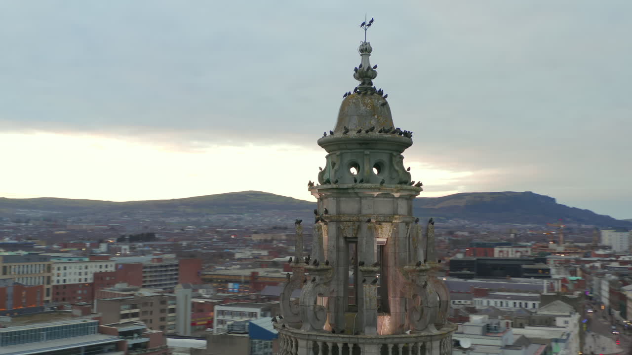 Drone circling ornate crown of Belfast City Hall dome with gathered birds against cityscape