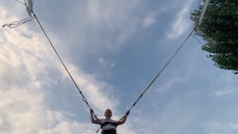 Looking-up-at-young-little-girl-having-fun-jumping-and-flipping-tied-with-harness-and-elastic-ropes-on-trampoline