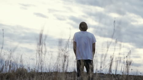 dolly shot in tall grass of man with hands in pockets staring at sunset sky