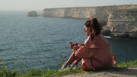 mujer usando el teléfono en un acantilado con vistas al mar