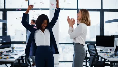 two happy businesswomen celebrating a goal achievement in the office, throwing confetti in the air and clapping hands, expressing joy and excitement for their success