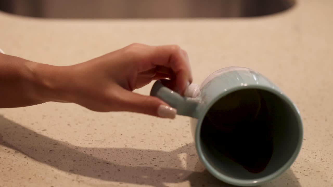 A mug tips over, spilling coffee onto a countertop. Warm lighting highlights the spreading liquid