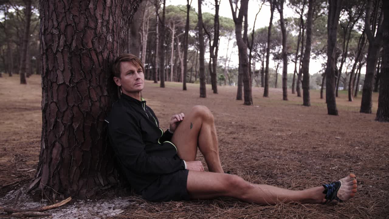 Man with leg out against tree alone in forest - depressed