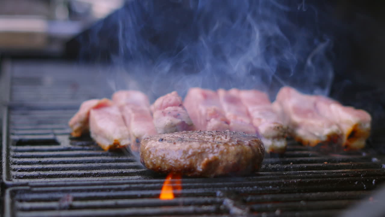 Wide View of BBQ with Beef Burger Being Flipped with Fire Flames Erupting from Below in Slow Motion. Barbecue Summer Cooking Food.