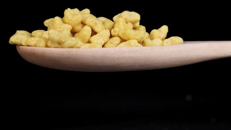 star-shaped cereal pieces fall from a wooden spoon against a black background, captured in slow motion with dramatic lighting