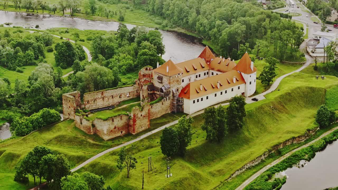 Ancient red-roofed Bauska Castle lies on green hilltop between river bends