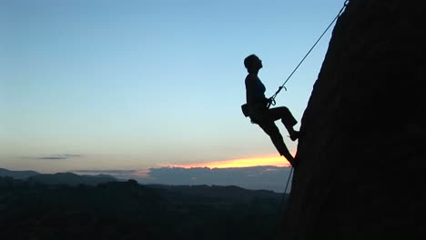 longshot of a rock climber silhouetted against a goldenhoursky rappelling down a cliff