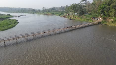 aerial footage shows a wooden bridge spanning the progo river, passable by motorbikes. as a link between the villages of bantul and kulonprogo.