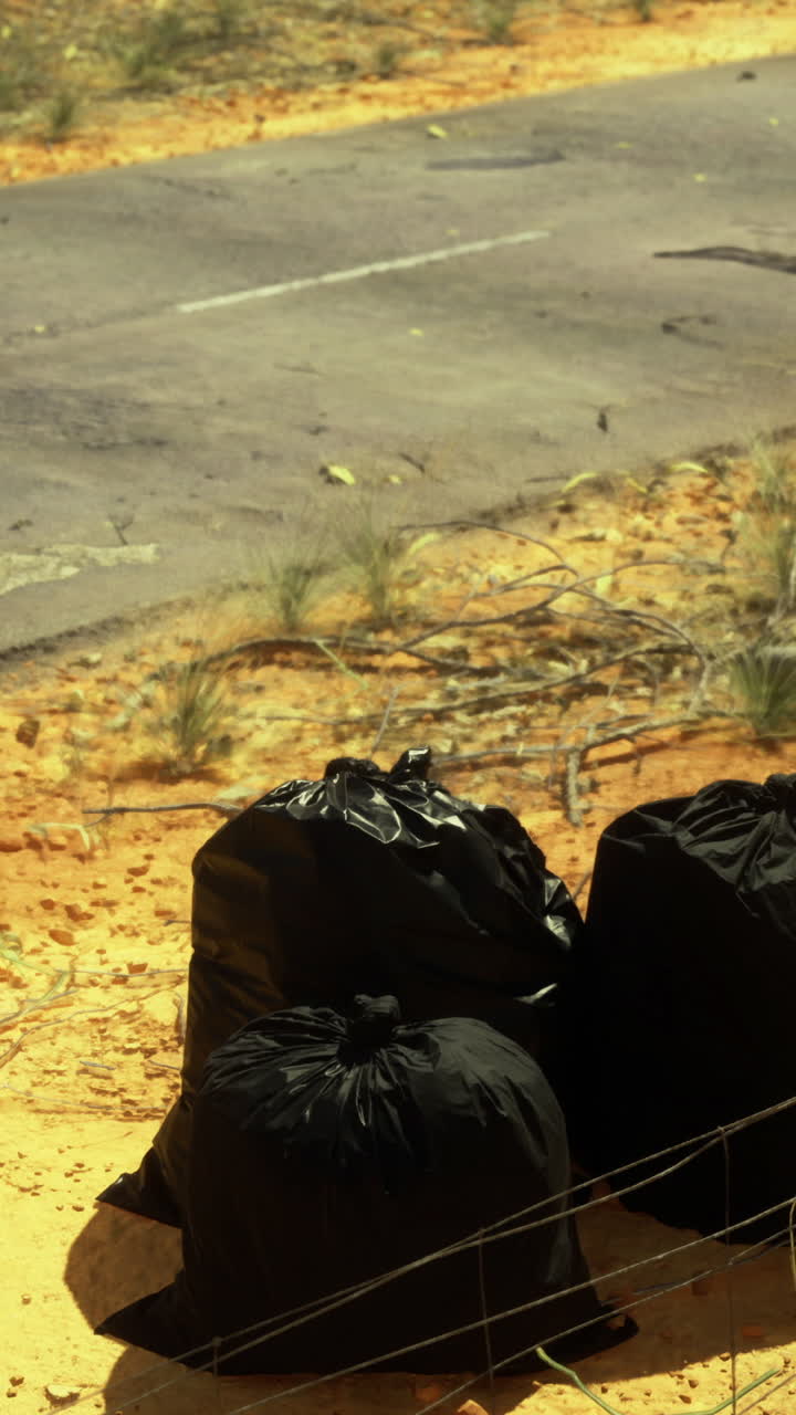 Sacchi della spazzatura lasciati lungo una strada deserta nel paesaggio arido della campagna.