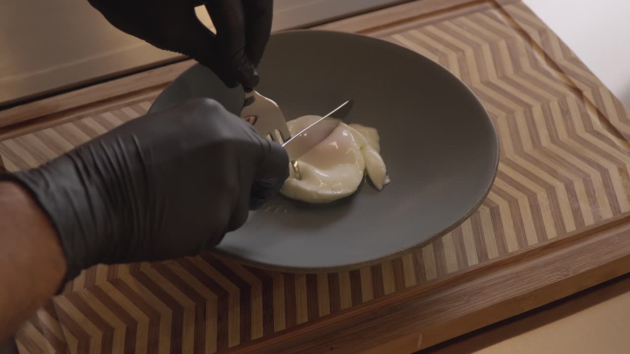 Gloved chef slicing soft boiled egg on ceramic plate