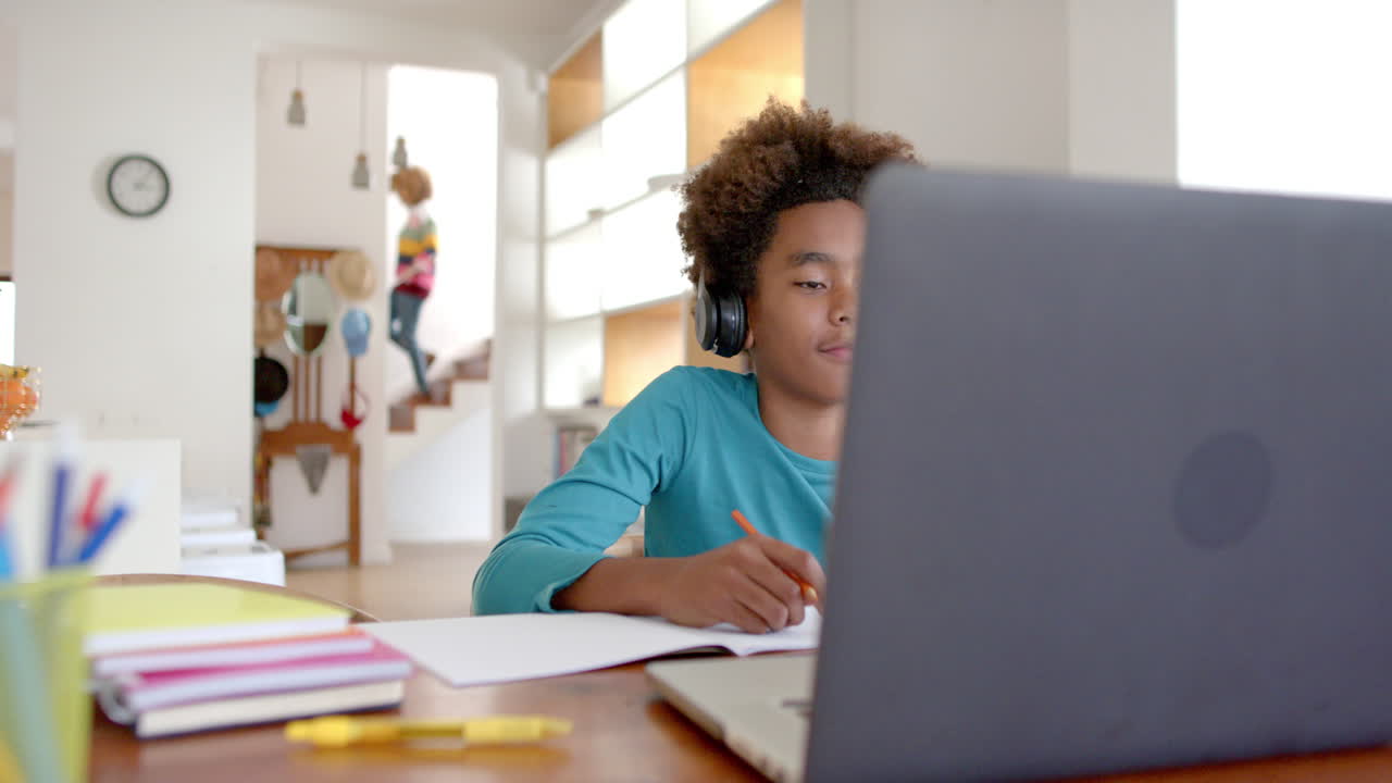 African american boy wearing headphones, using laptop for online class, slow motion