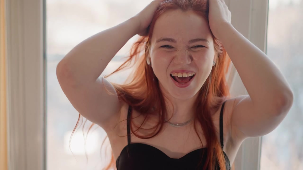 活発な動きを楽しむ笑顔の少女。日差しが差し込む窓のそばで、楽しそうに踊る陽気な若い女性。日当たりの良い窓辺で元気に踊りながら明るく微笑む活発な若い女性