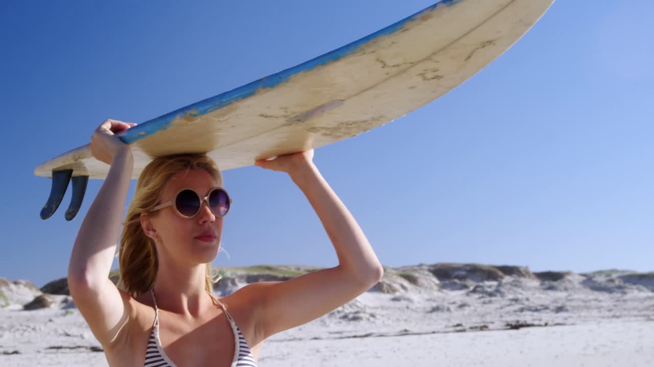 해변 에서 머리 위 에 서프보드 를 들고 있는 젊은 여자