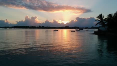 Aerial-shot-at-low-altitude-flying-towards-sun-in-sunrise-passing-over-small-boats-anchored