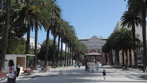 a sunny day in a palm tree-lined plaza with people strolling and children playing