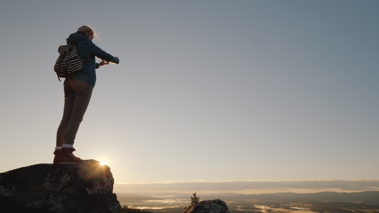 una mujer activa toma fotografías de un hermoso paisaje a sus pies de pie en la cima de una montaña tr