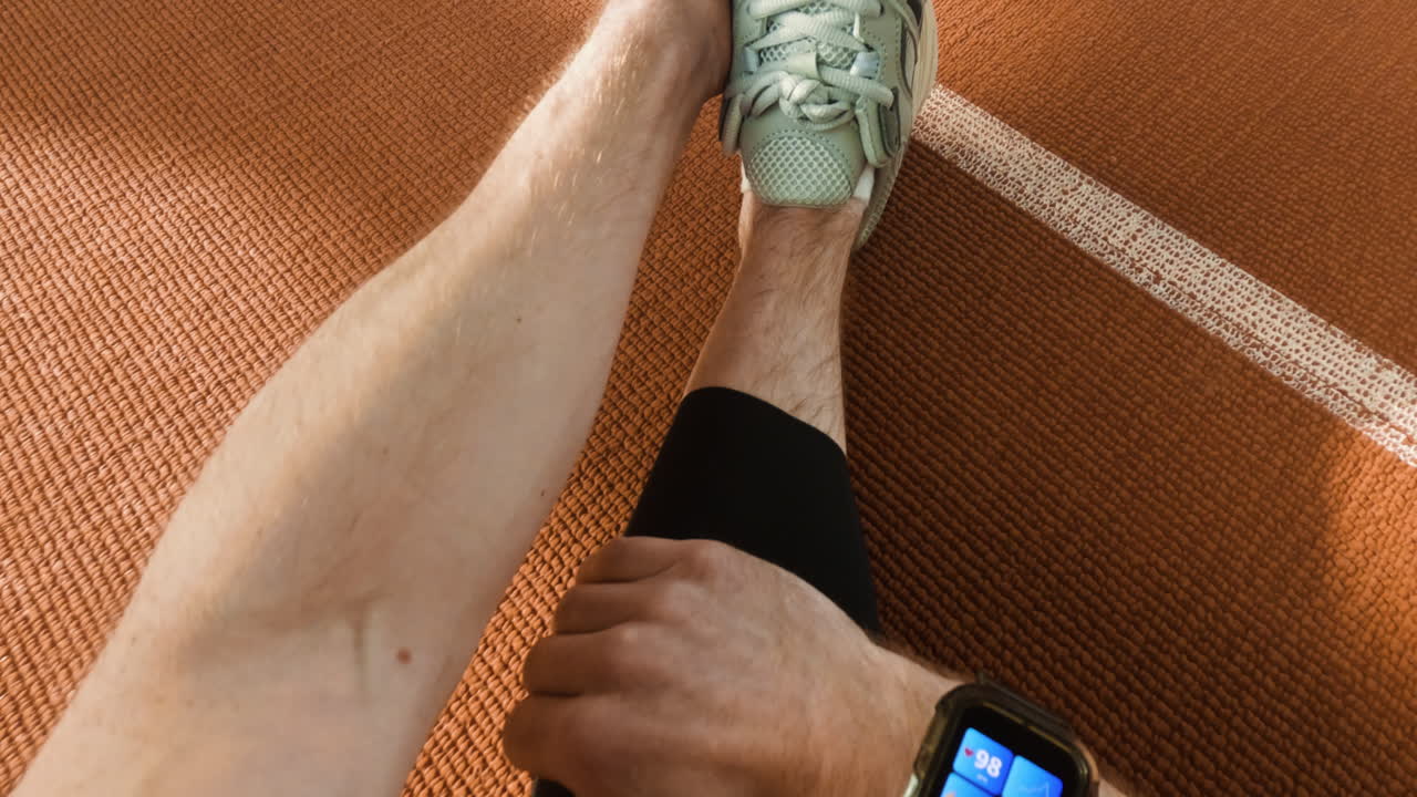 A person's arm and hand on a textured orange sports court with white lines, and an abstract view of the court