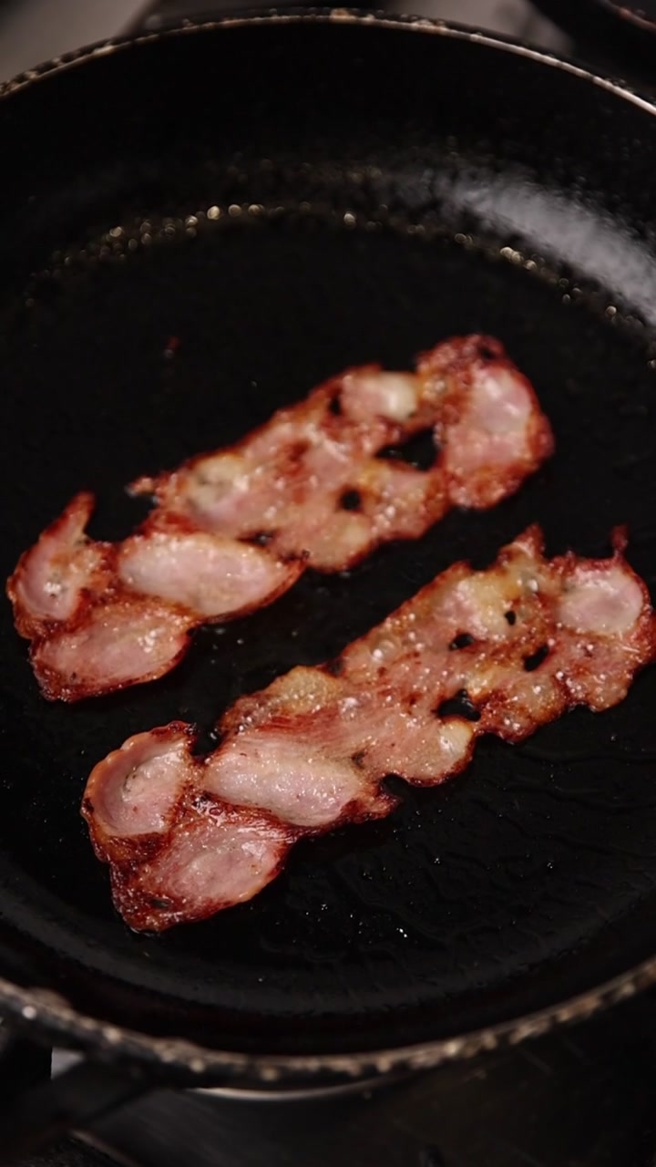 Due fette di pancetta che friggono in una padella calda