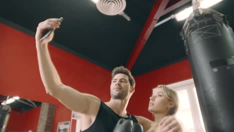 una pareja alegre abrazándose para una selfie móvil en el gimnasio.