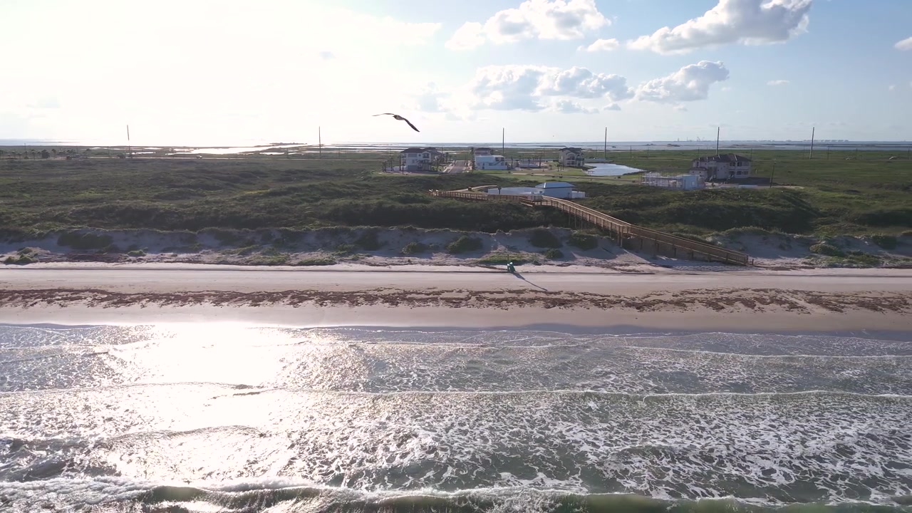 Et droneopptak fanger bølger som forsiktig slår inn mot land nær Port Aransas nede ved Texas-kysten, like utenfor et nabolag med en brygge som strekker seg fra samfunnet til sanddynene og stranden