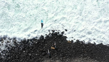 Toma-De-Vista-Superior-De-4k-Drone-De-Un-Surfista-Saltando-En-El-Agua-Con-Su-Tabla-De-Surf-Desde-La-Costa-Rocosa-En-Lennox-Head,-Australia