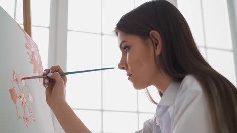 woman draws red flowers on canvas sitting near large window