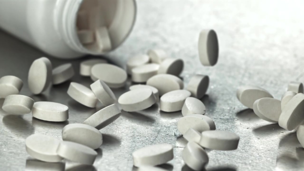Pillole ovali bianche che cadono da un flacone di medicinali al rallentatore