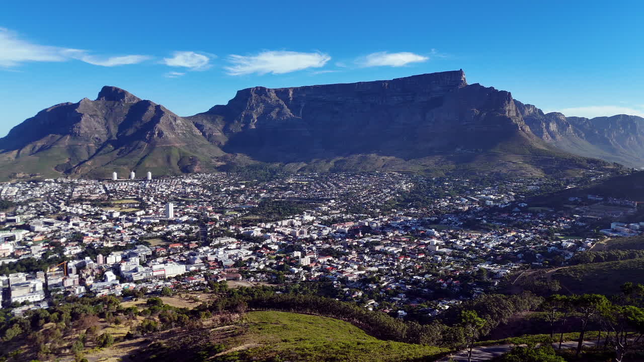 Cinematic aerial view of Table Mountain and Cape Town cityscape, showcasing rugged cliffs, urban sprawl, and South Africa’s iconic natural landmark under clear blue sky