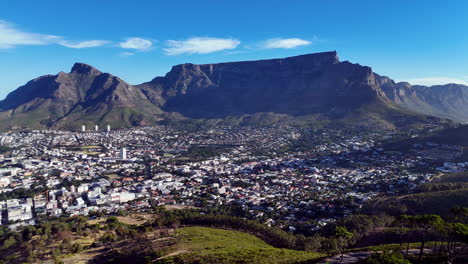 cinematic aerial view of table mountain and cape town cityscape, showcasing rugged cliffs, urban sprawl, and south africa’s iconic natural landmark under clear blue sky
