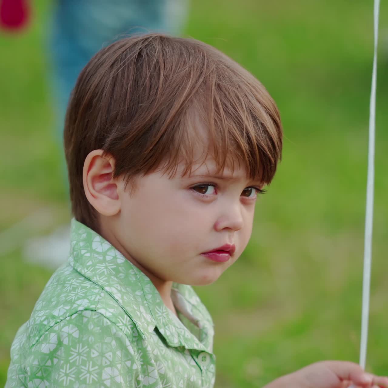 Portrait of baby boy on green nature background. Cute little boy sitting on the green grass and holding rope with a balloon.
