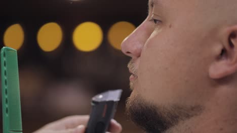 barber cutting beard using electric trimmer, makes haircut for groom man customer at barber shop