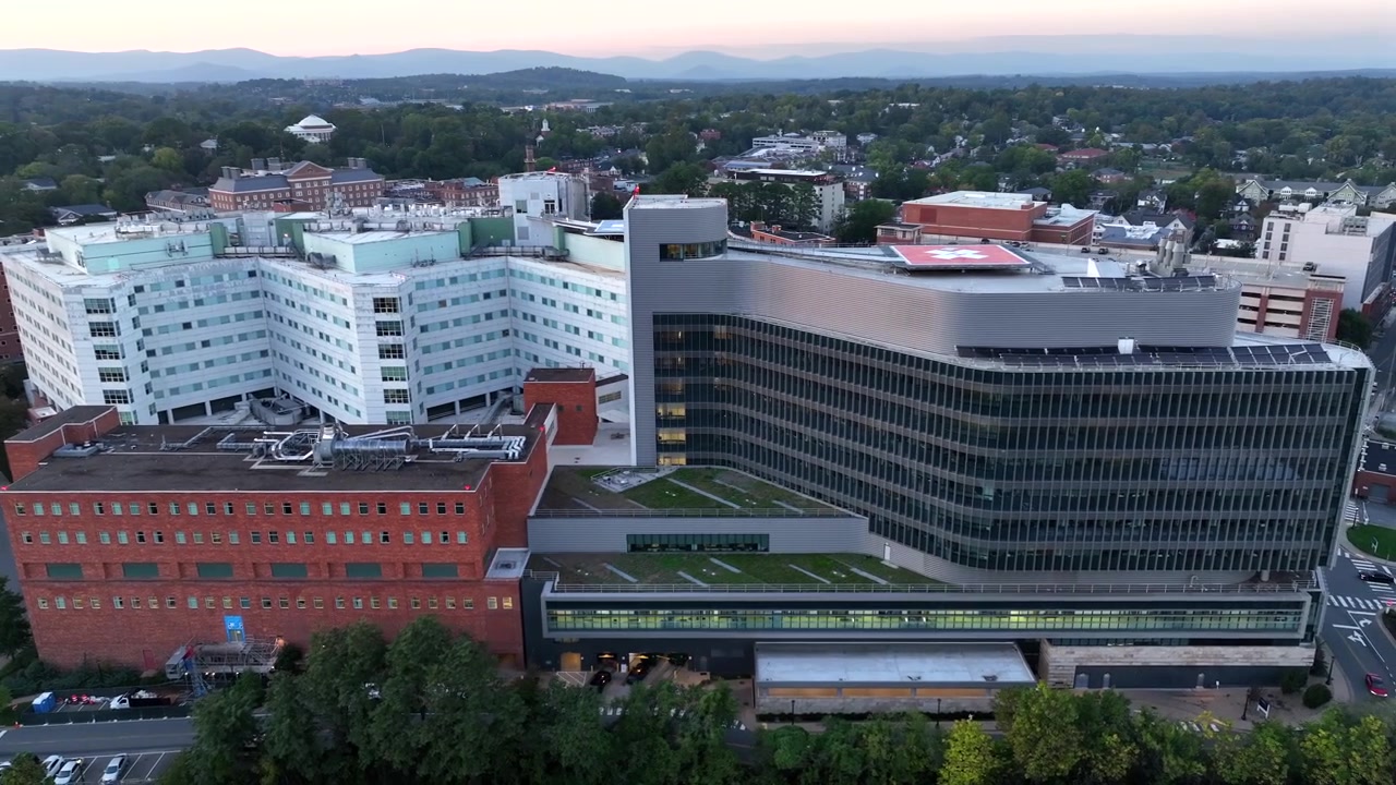 Imagem aérea orbital do Hospital Universitário UVA Health na cidade de Charlottesville. Manhã cedo em uma cidade americana ao longo dos trilhos do trem. Árvores verdes e montanhas durante o outono. Plano geral.