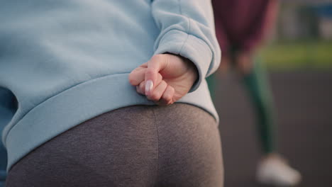 close up waist view of a lady in a cyan sweater, slightly bent, making a hand gesture, with a blurred view of other ladies in the background engaged in an exercise routine