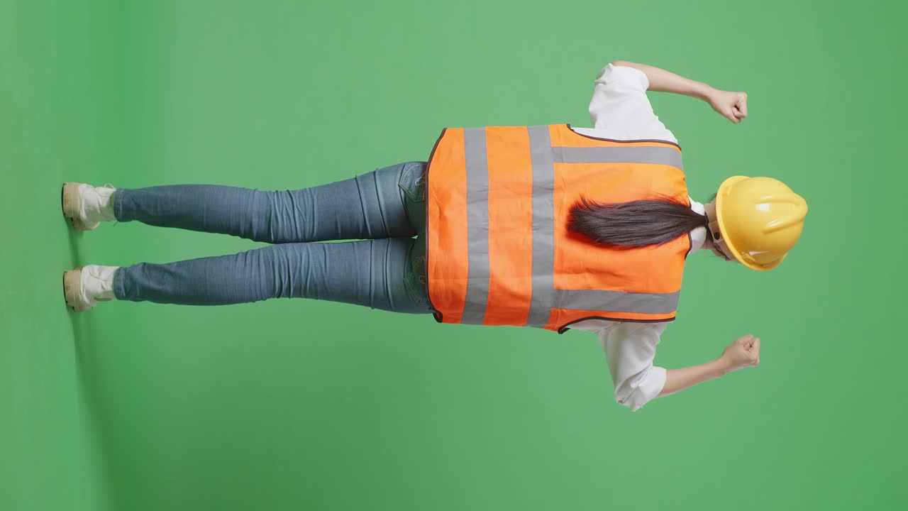 vista trasera completa del cuerpo de una ingeniera con casco de seguridad levantando las manos celebrando mientras trabaja en el estudio de fondo de la pantalla verde