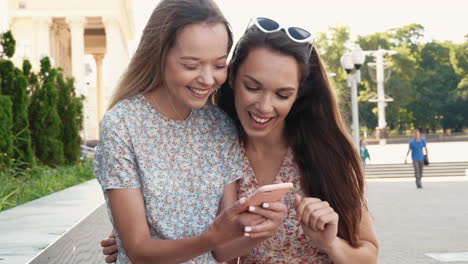 dos mujeres mirando un teléfono inteligente al aire libre