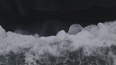 Aerial-top-view-of-ocean-waves-crashing-on-Iceland-Sólheimasandur-black-sand-beach