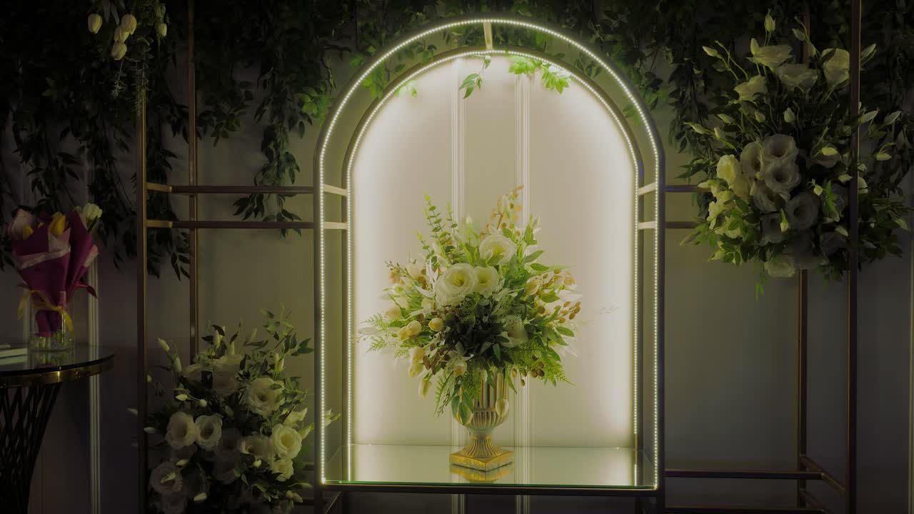 Lussuose decorazioni di fiori bianchi, disposte in un unico bouquet in un vaso d'oro all'interno di un'arcata luminosa, ripresa in tracking.