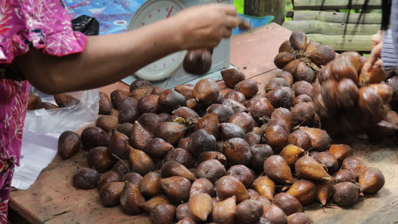 인도네시아 여성이 은 전통 시장에서 살락이나 과일을 선택하고 있습니다.