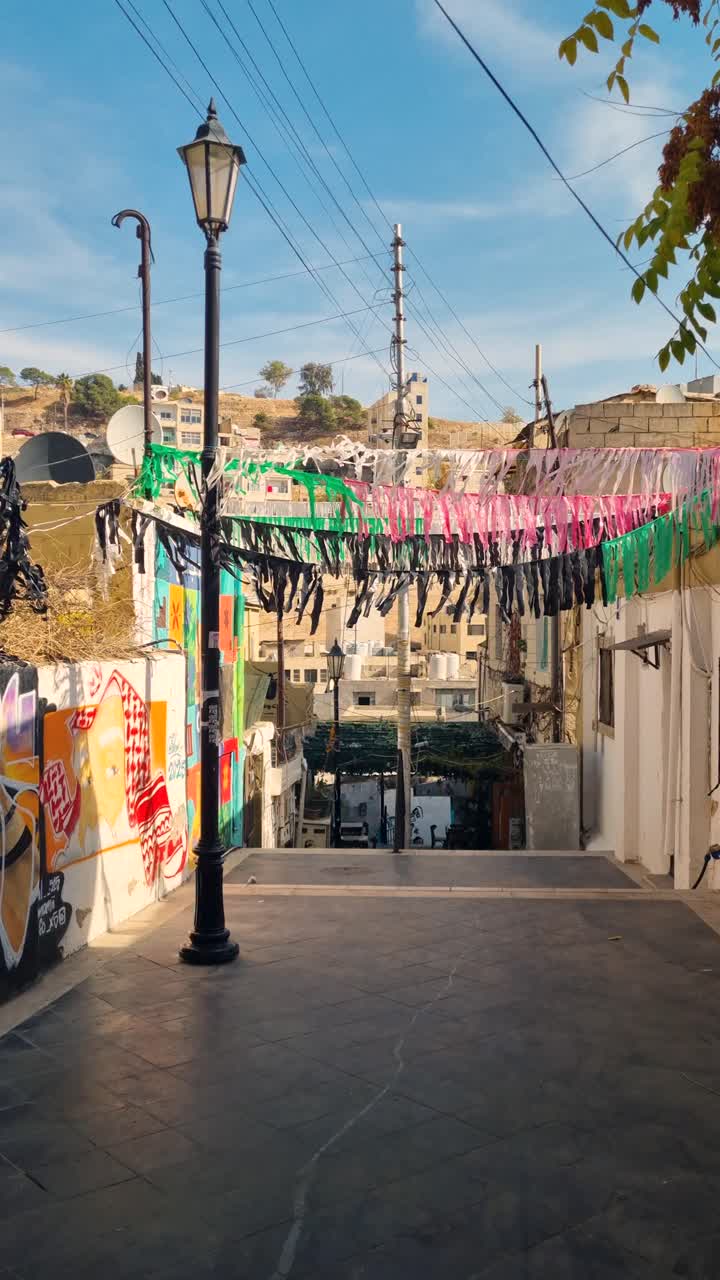 Vista verticale di Al Kalha Stairs nel centro di Amman, in Giordania. Ghirlande colorate con i colori nazionali ondeggiano al vento sotto un cielo blu e soleggiato, mettendo in risalto la vivace street art e la vita locale.
